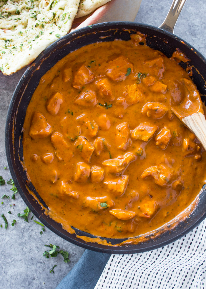 Butter Chicken cooked in skillet stirred with a spoon then sitting on top of a table to serve