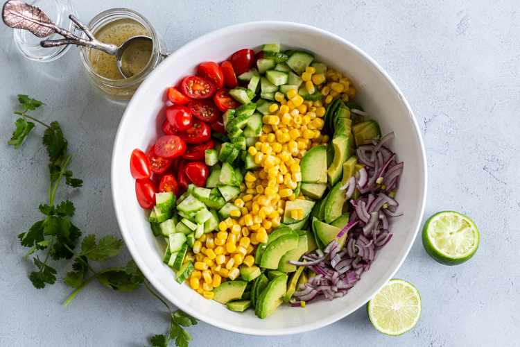 Corn tomato Avocado salad in a bowl with dressing next to it