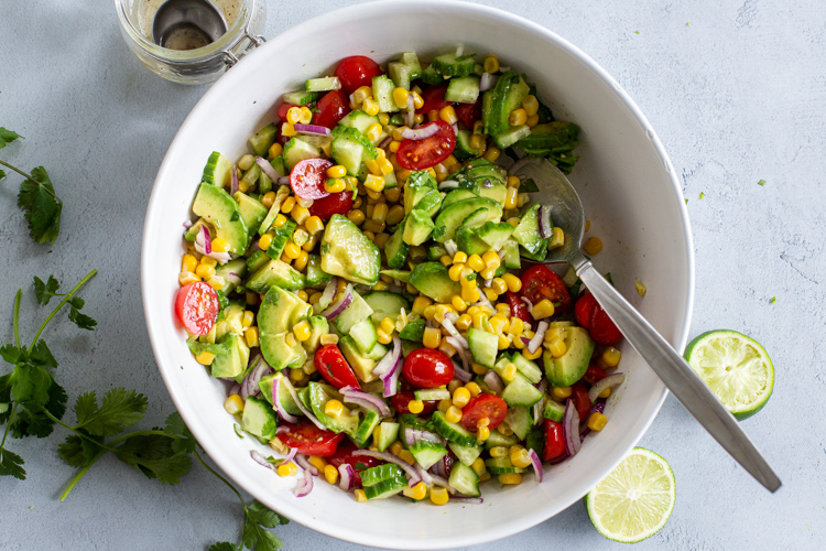Corn tomato Avocado salad in a bowl with dressing next to it
