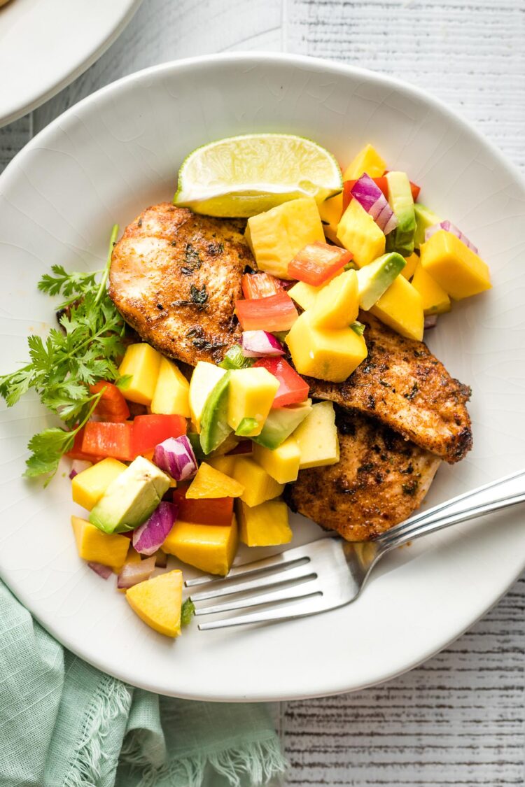 White plate with a serving of jerk chicken and mango avocado salsa.