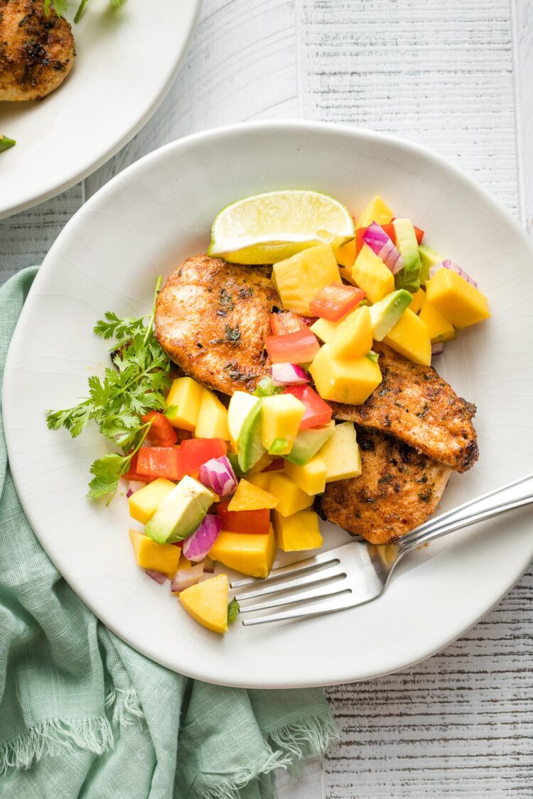 White plate with a serving of jerk chicken and mango avocado salsa.