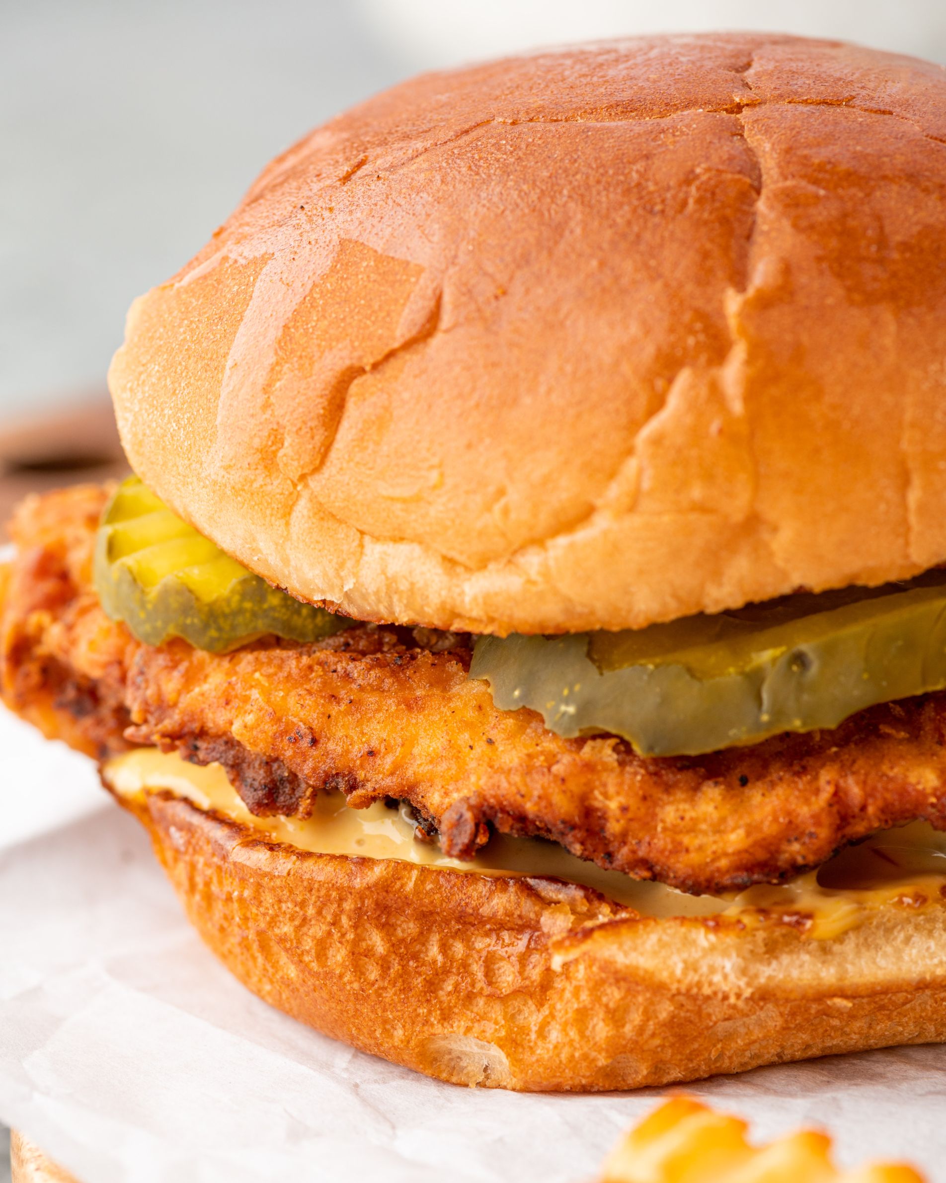 Crispy chicken sitting between hamburger buns with sauce and pickles.