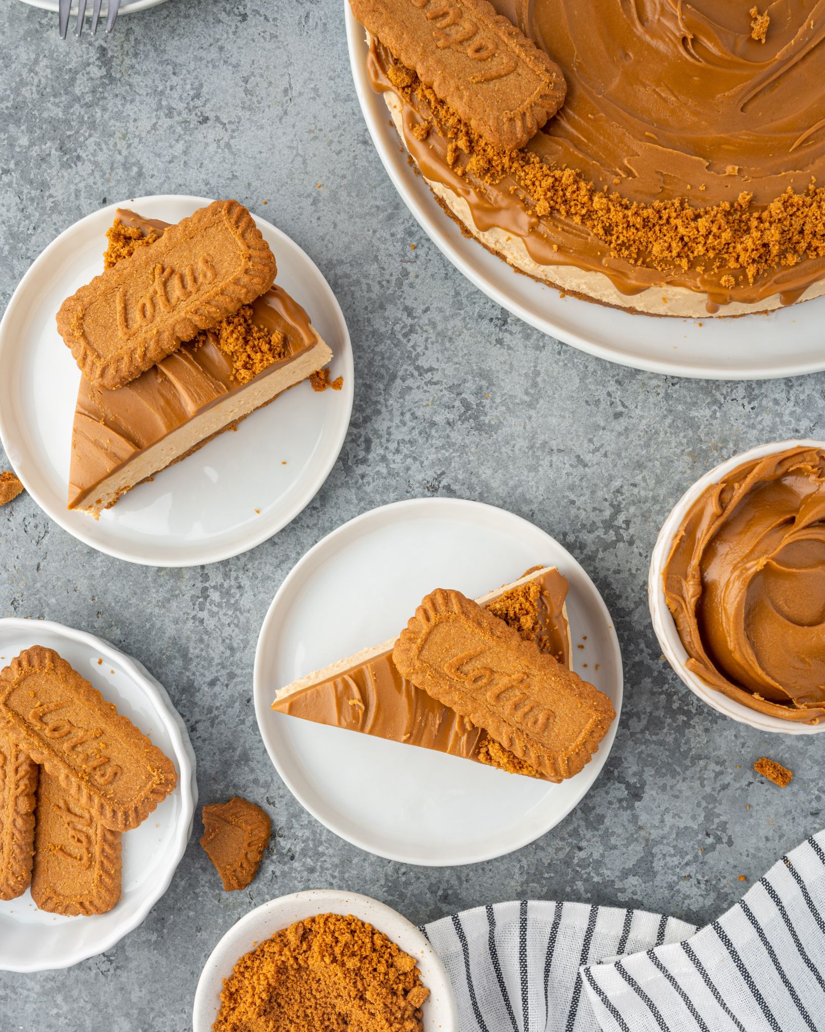 Slices of no bake cheesecake topped with Biscoff cookies on small plates.