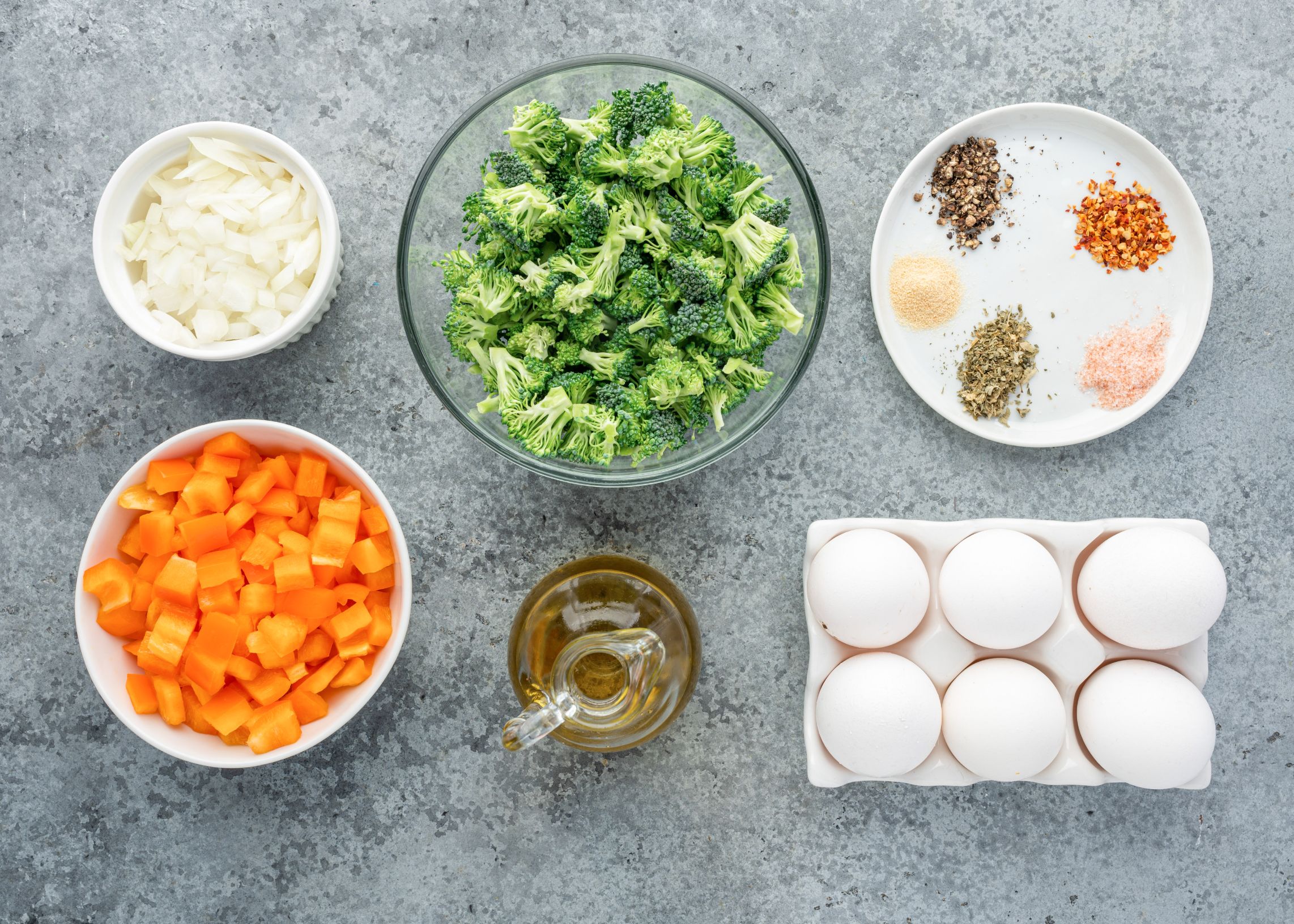Eggs, chopped bell pepper, broccoli, onion and spices divided into bowls.