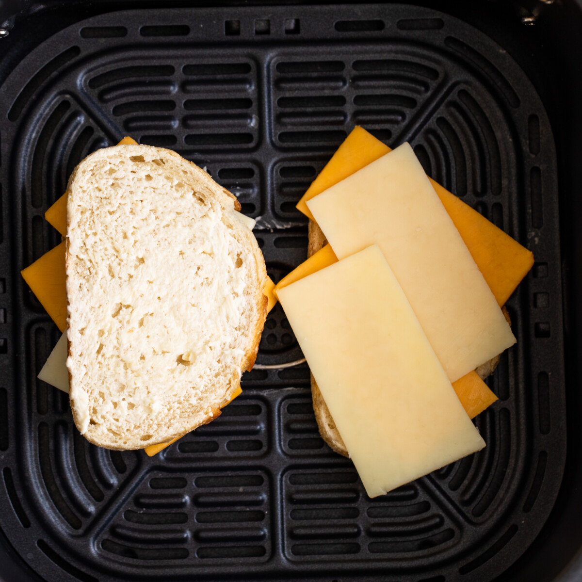 Adding cheese to sandwich bread in an air fryer.