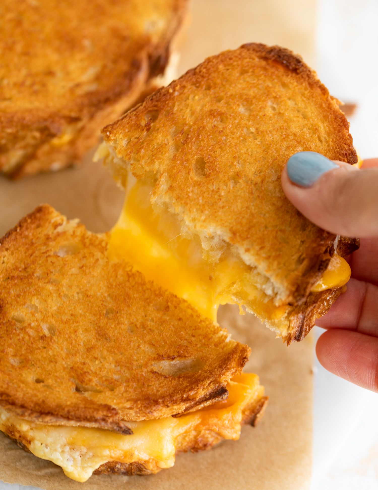 Hand pulling two halves of an air fryer grilled cheese apart.