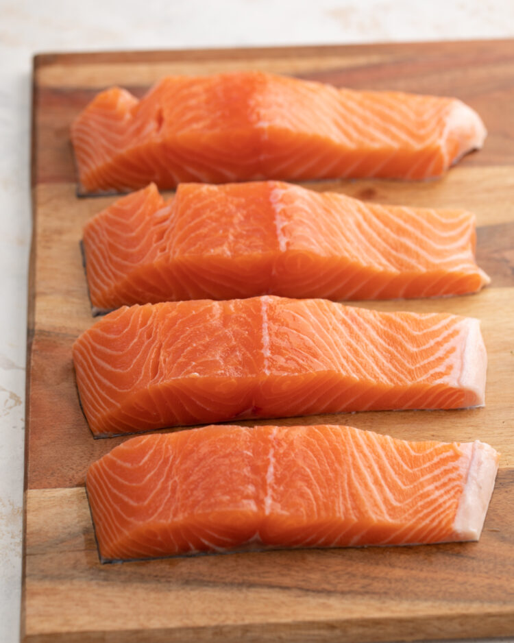 Four fillets of salmon on a cutting board.