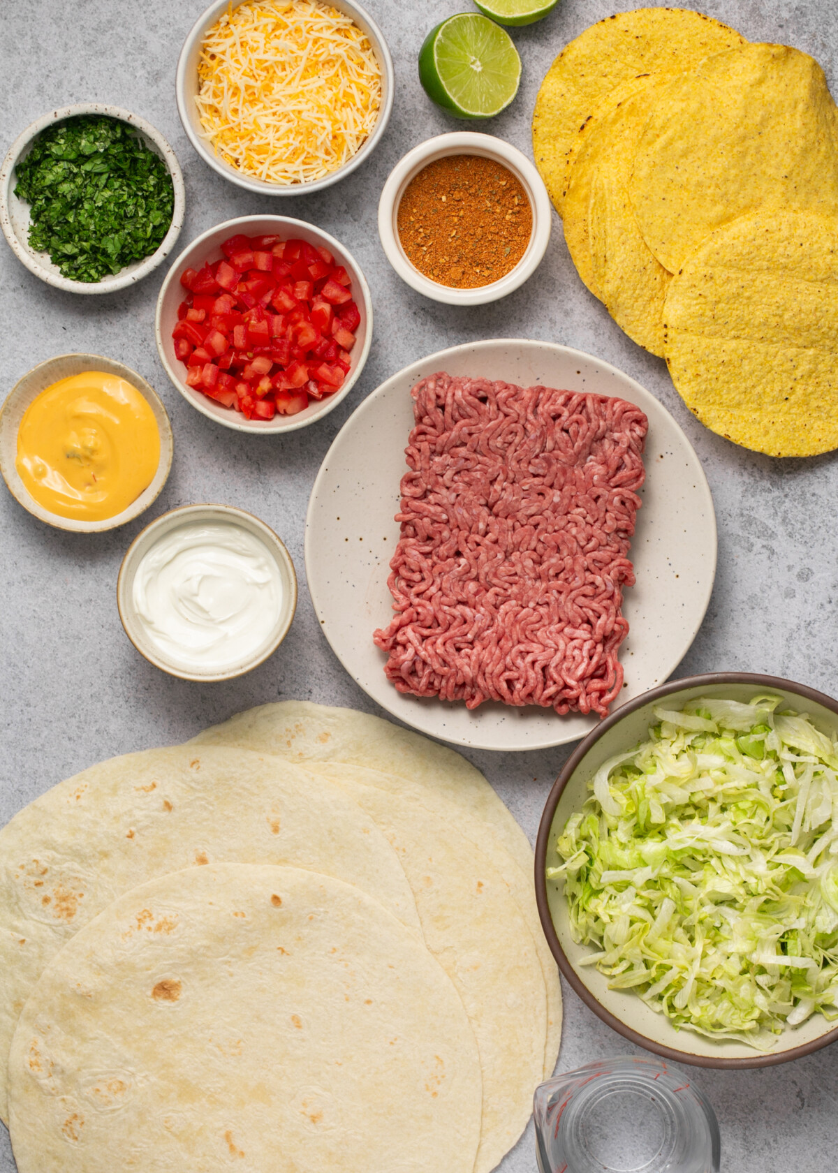 Ingredients needed for recipe including beef, tostadas, queso, cheese, tomatoes, taco seasoning, lime, cilantro, tortillas, lettuce, and sour cream