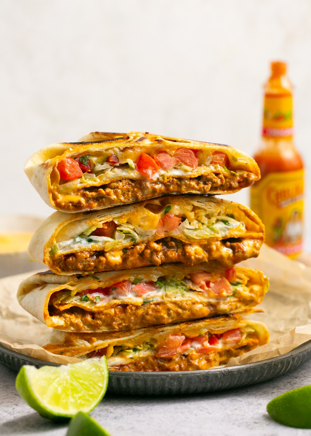 Beef crunchwrap supremes cut in half and stacked up with a bottle of hot sauce in the background. 