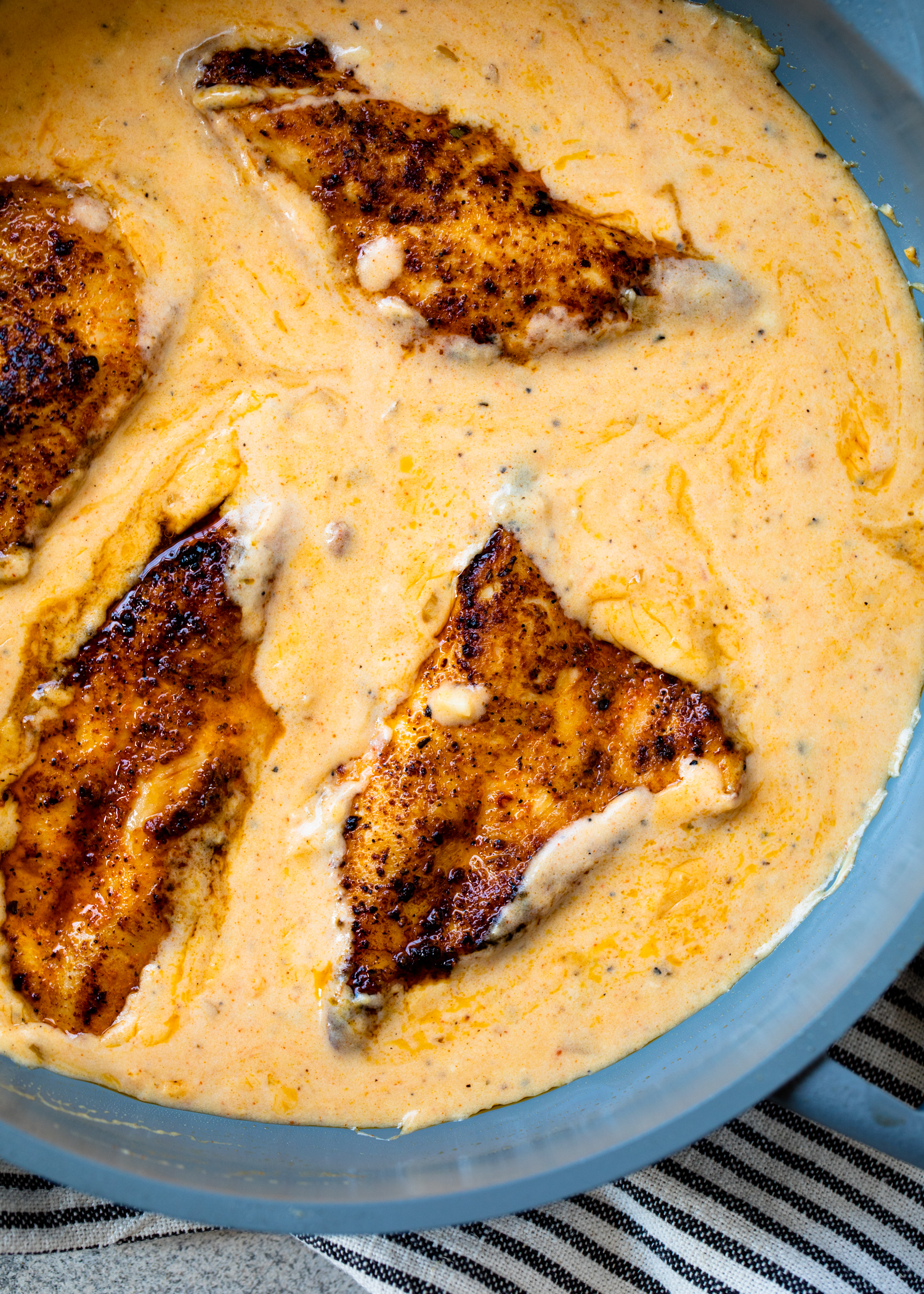 Adding cooked chicken into creamy sauce in a pan.