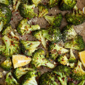 Roasted broccoli on a pan with lemon wedges.