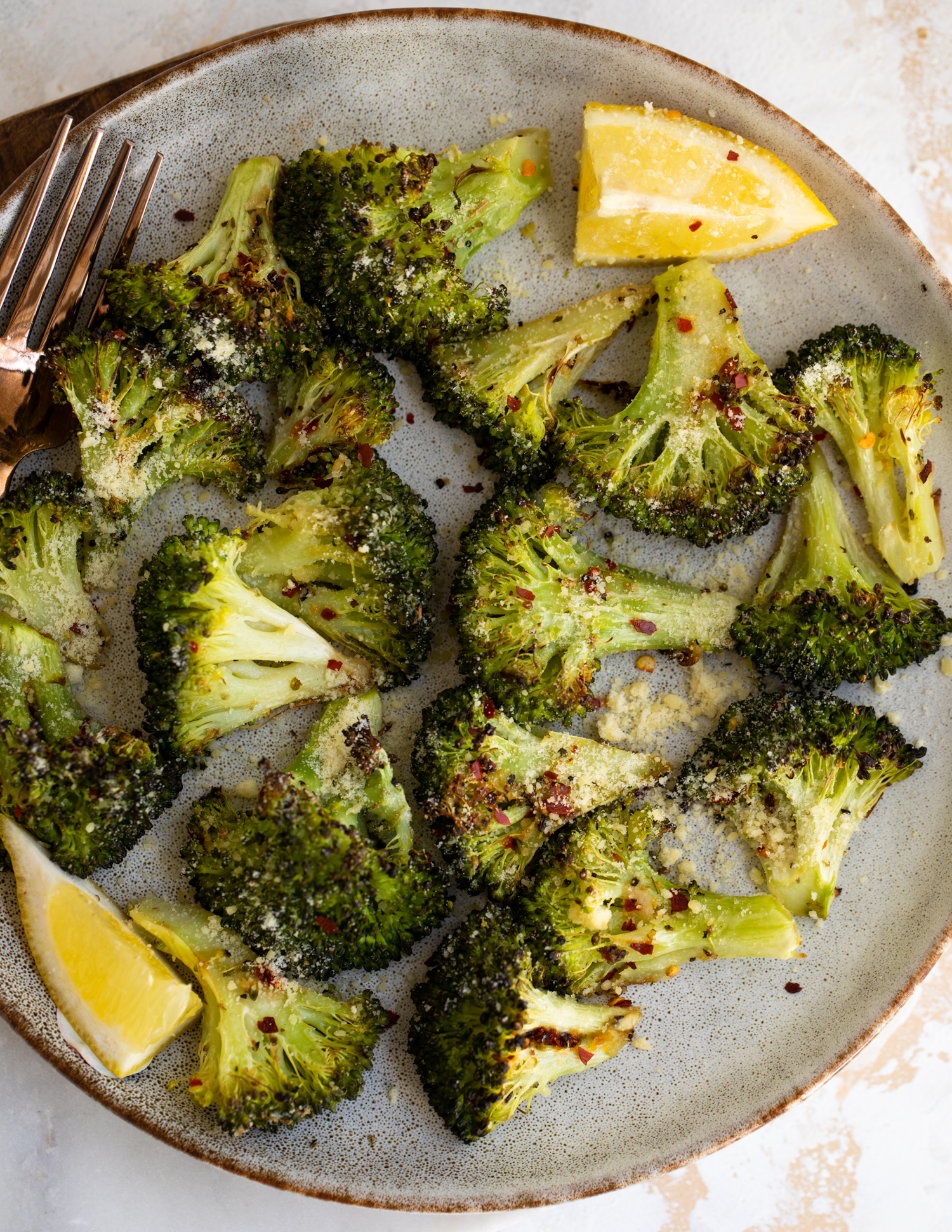 Roasted broccoli on a plate with lemon wedges.