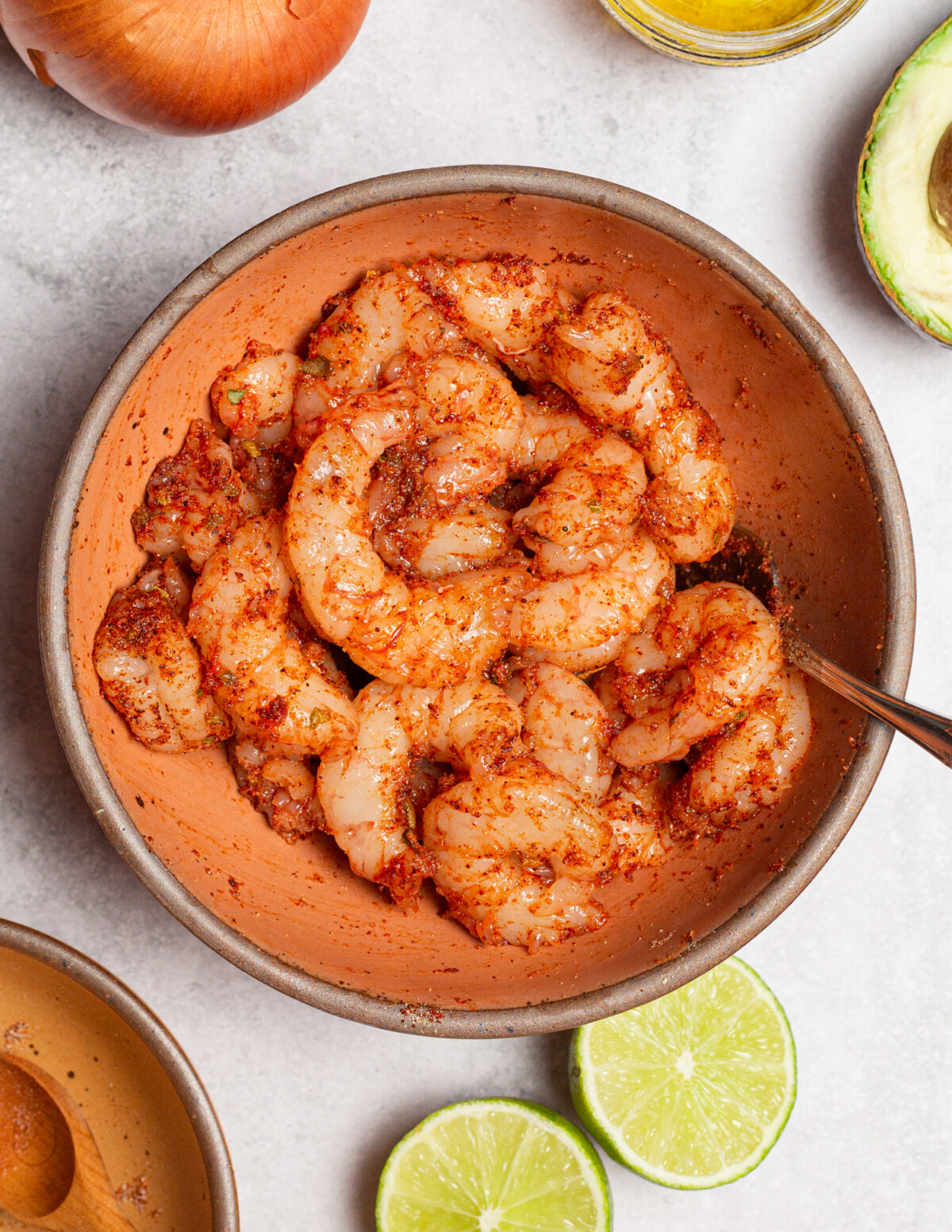 Seasoning raw shrimp with spice mix in a small bowl.